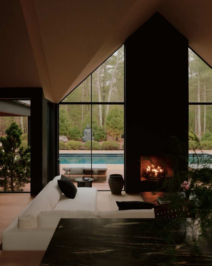 Living room with a black timber chimney, a fire lit and a glass gable facing the pool at Bali House, East Hampton