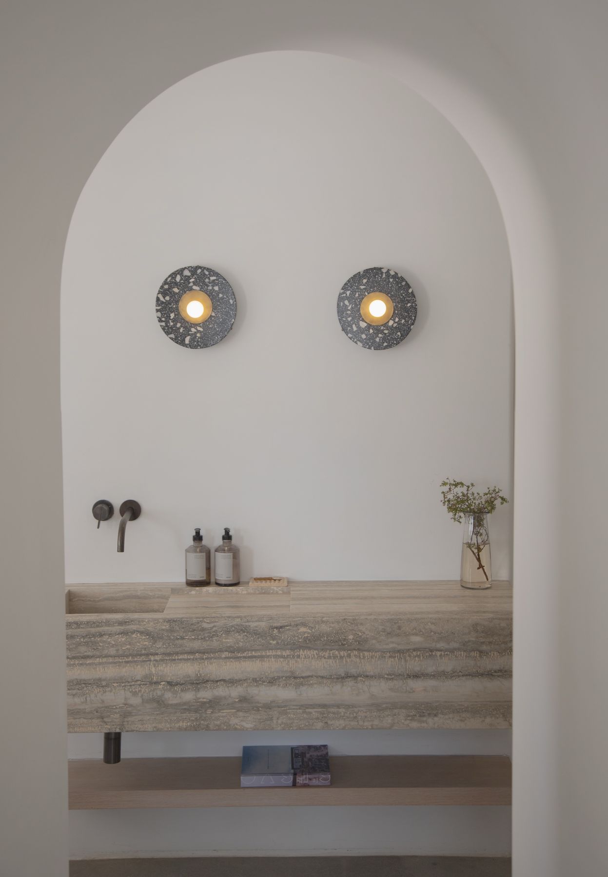 Arched plaster alcove with a travertine vanity and two sconces at Le Chacuel, Yucca Valley