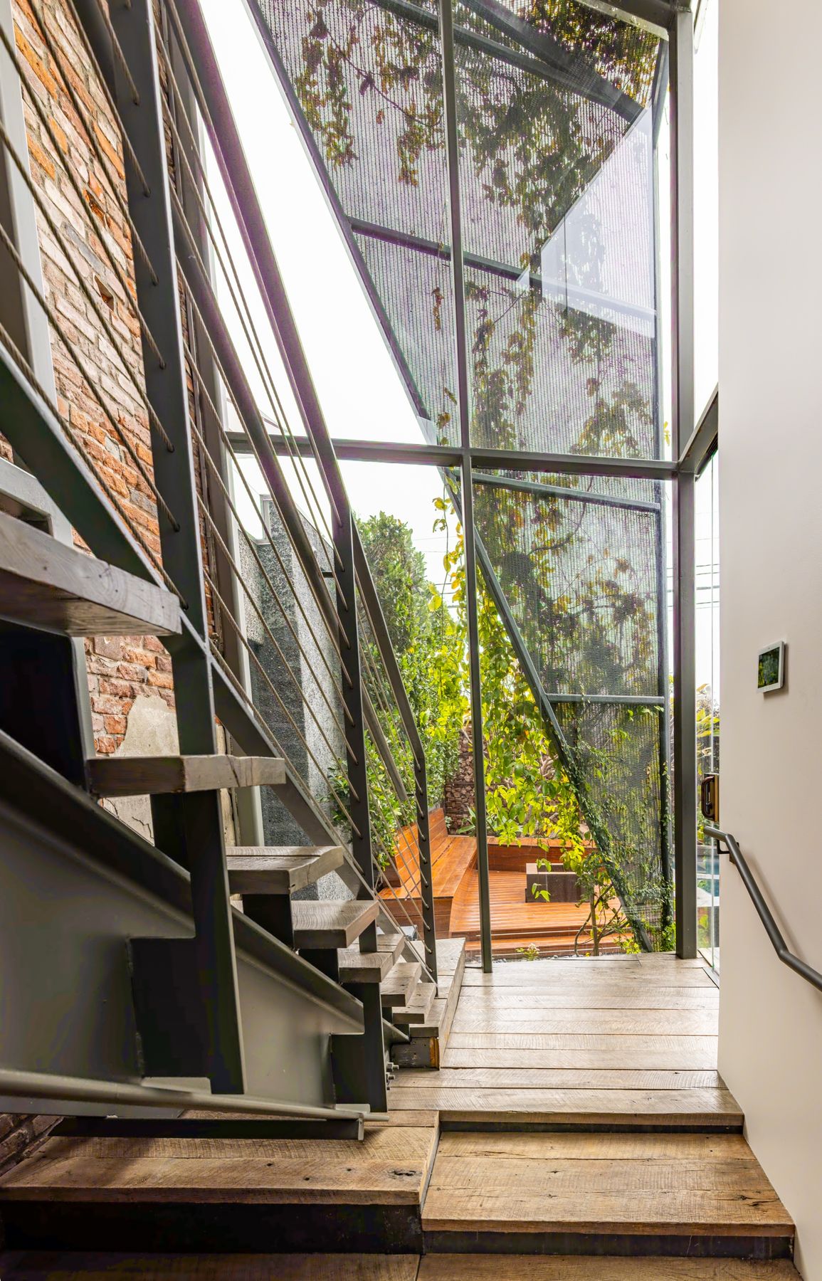 Steel stair with wood treads beside a glass atrium and a brick wall at Powell House, Venice