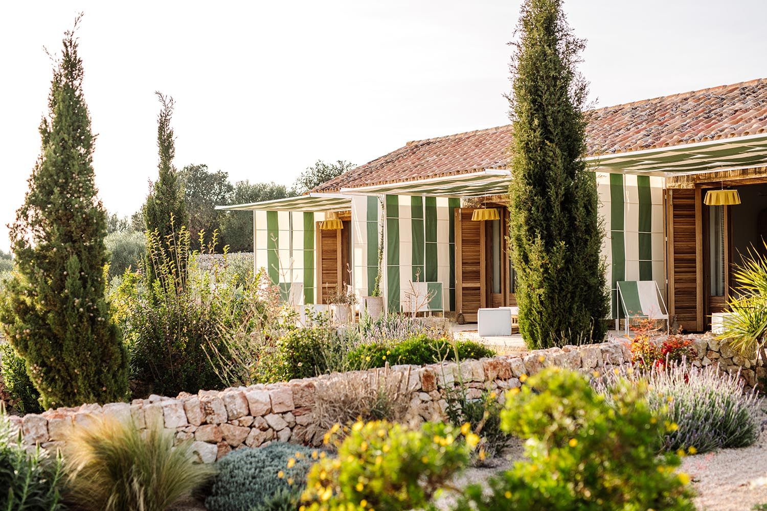 Whitewashed farmhouse with green shutters behind cypress trees and a dry-stone wall at Finca Amagatay, Menorca