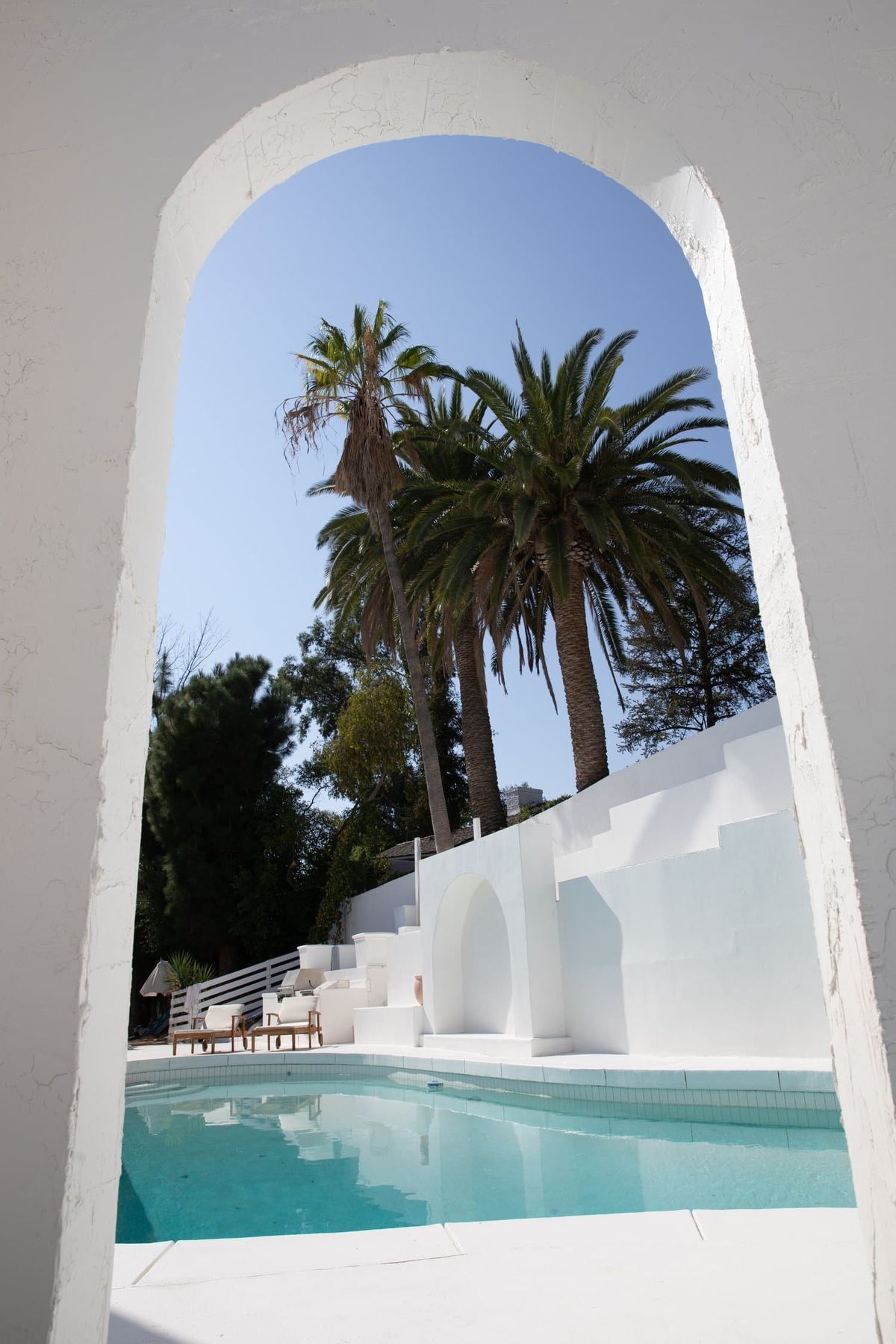 White plaster arch framing palms and the stepped pool wall at Castor House, Tarzana