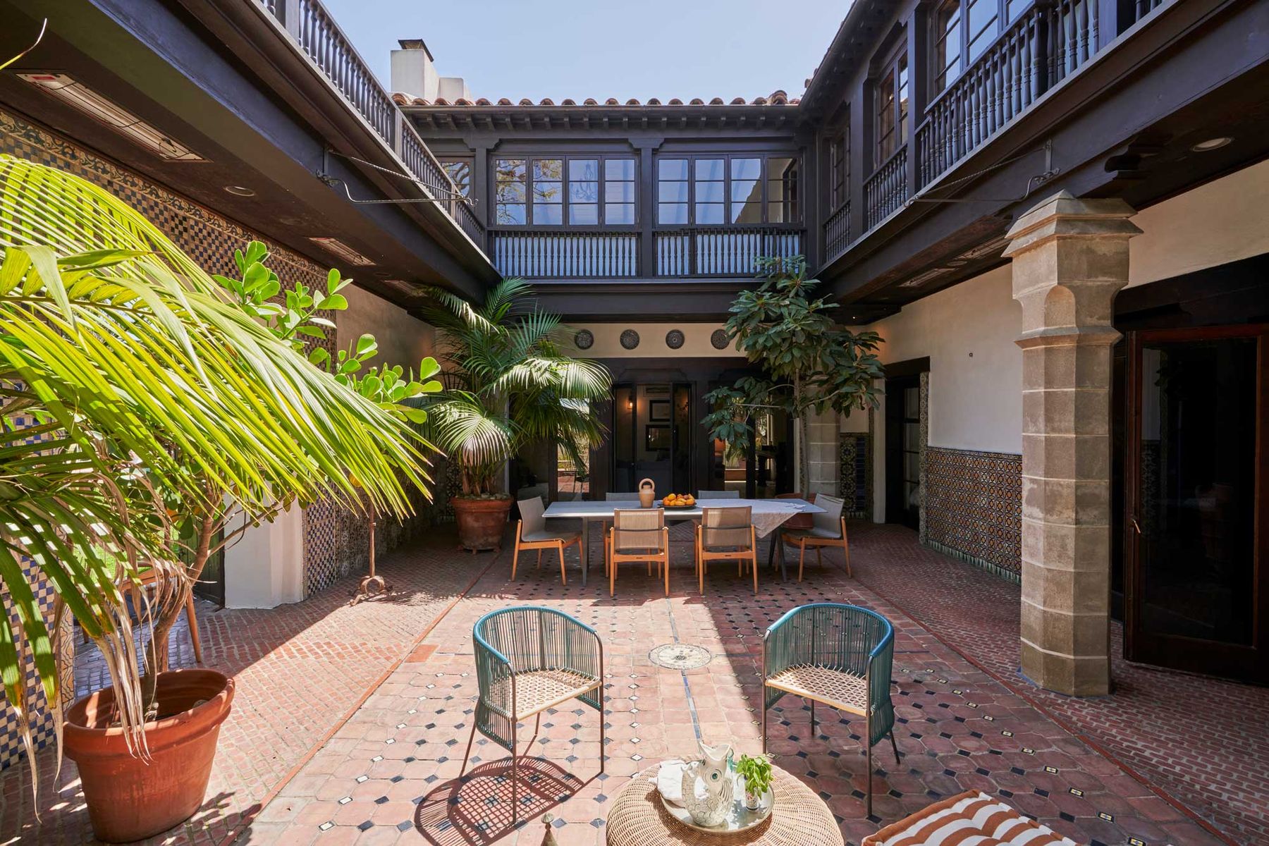 Brick-paved courtyard with carved wood balconies, palms and a dining table at Casa El Greco, Santa Monica