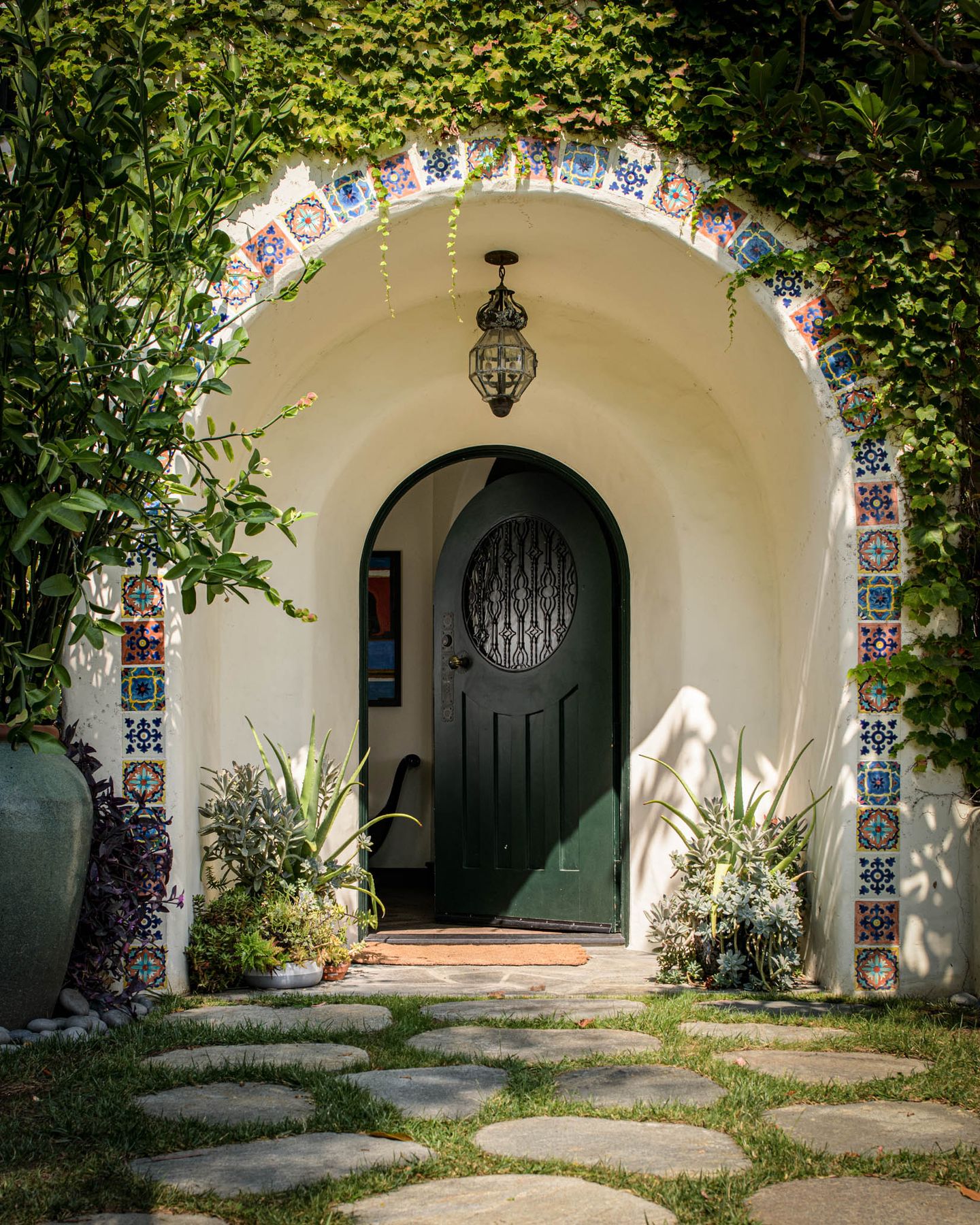 Arched front door with a painted tile surround and stepping stones at Kings Road Estate, West Hollywood