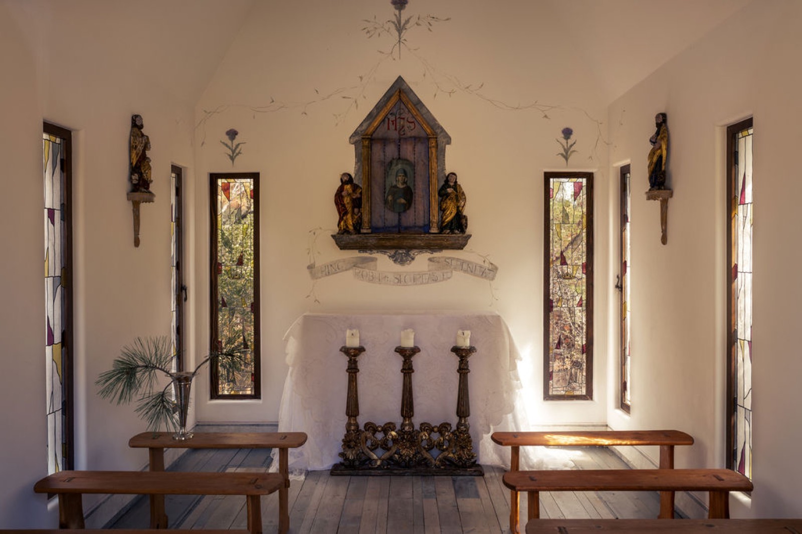 Chapel interior with a lace-draped altar, painted saints, stained glass and wooden pews