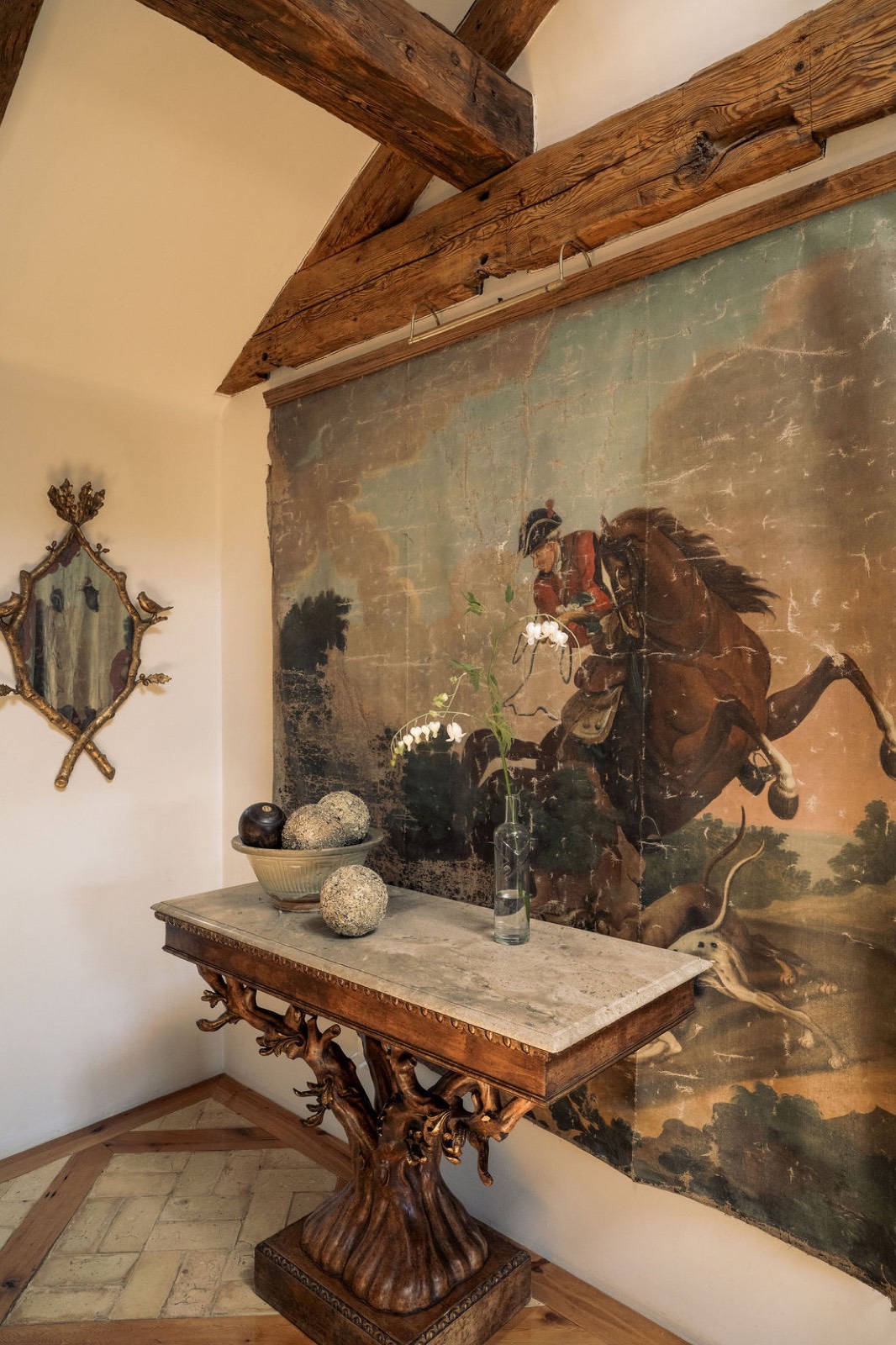 Entry hall with an antique hunt-scene canvas, carved tree console and timber beams