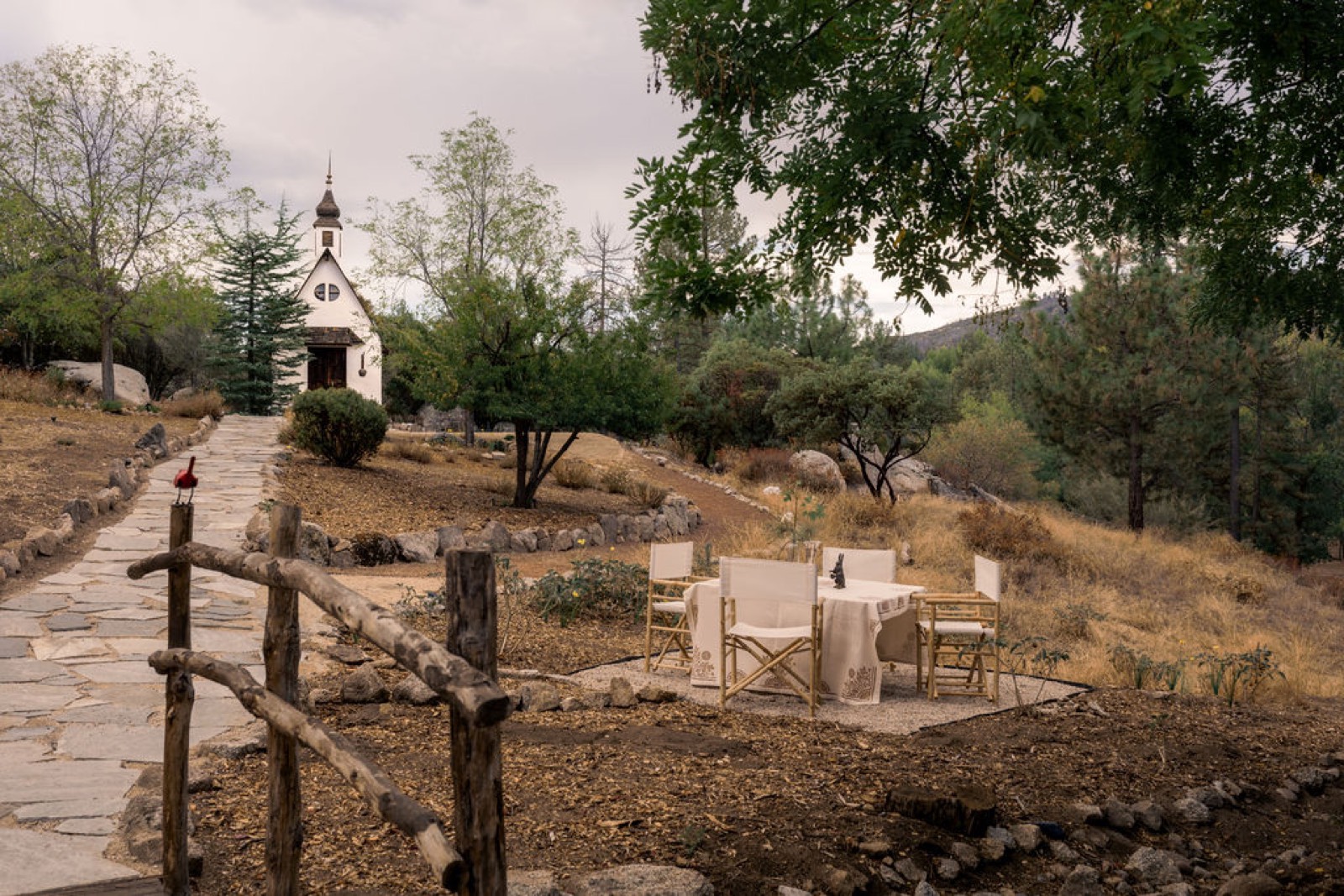 Flagstone garden path leading to the white chapel and its steeple, past a rustic fence and bistro table