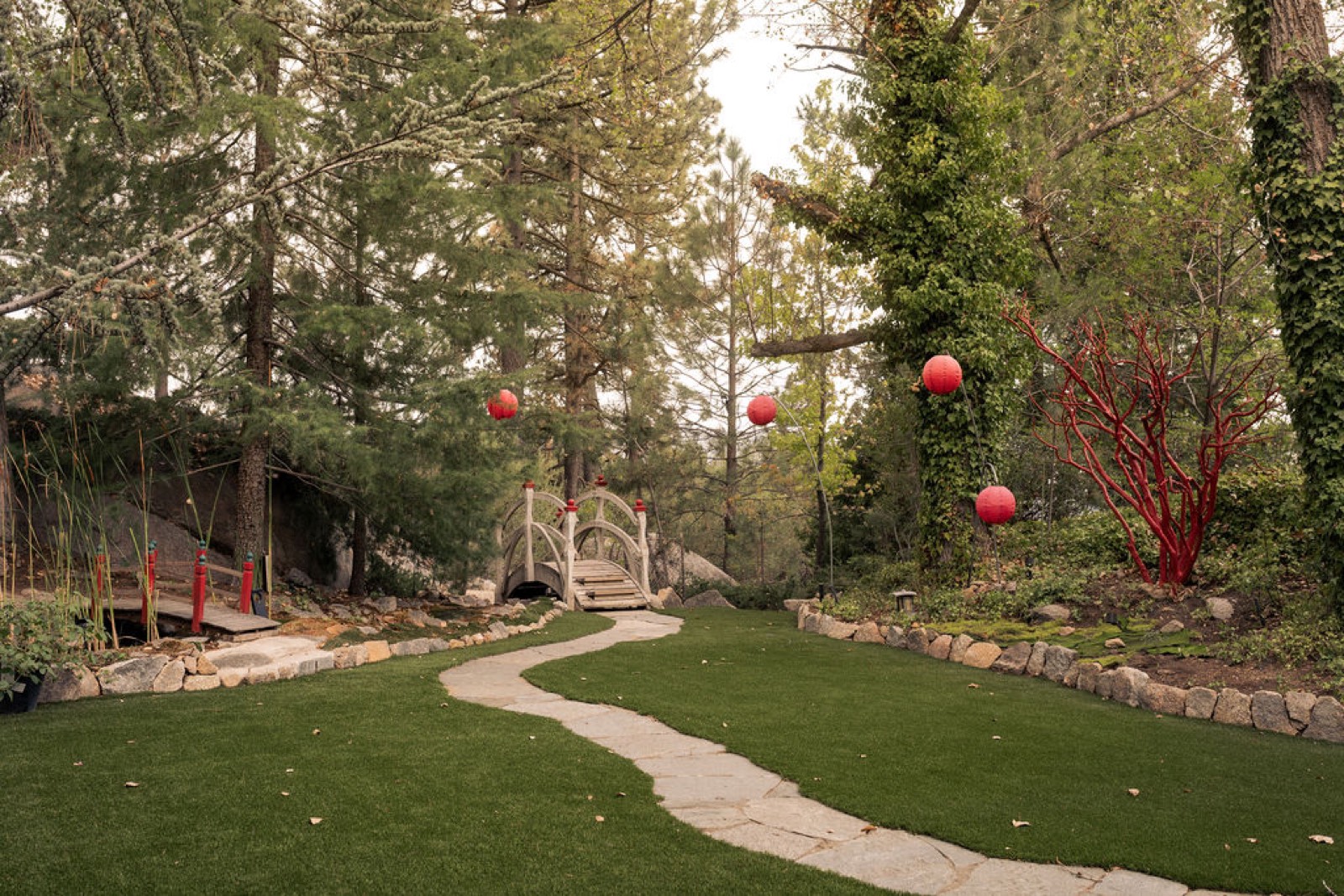 Arched footbridge strung with red paper lanterns over a flagstone path