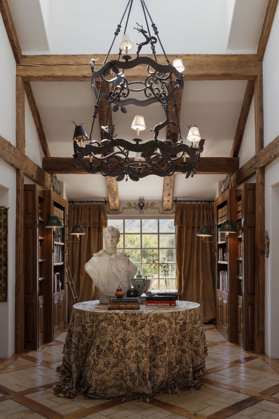 Double-height library hall with a wrought-iron stag chandelier, plaster bust and mountain window