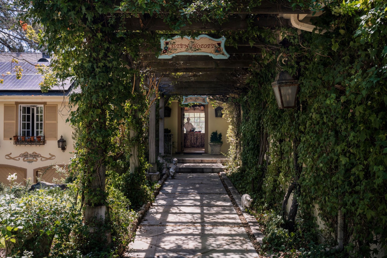 Vine-covered pergola walk to the front door of Chalet Tournesol under a painted Isten hozott sign