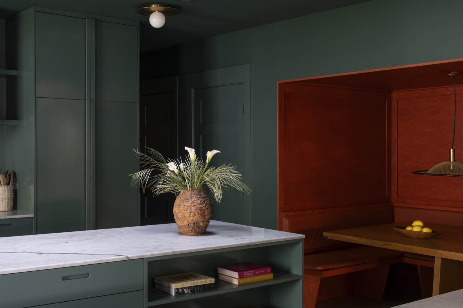 Kitchen with forest green cabinetry, a white marble island and a burnt orange banquette at Bowling House, West Hollywood
