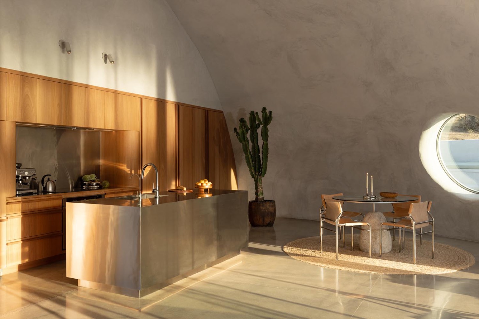 Kitchen with curved concrete walls, a steel island and a porthole window at Desert Dome, Pioneertown