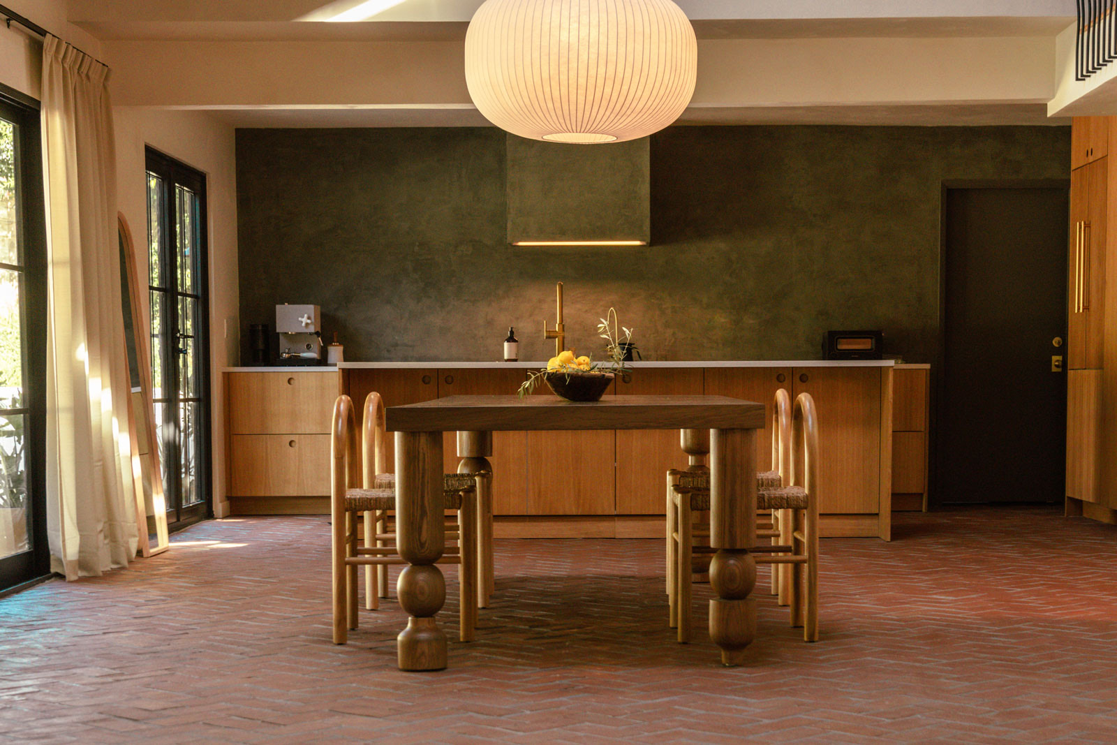 Hacienda Granada kitchen with olive plaster walls, terracotta herringbone floor, brass fixtures and sculptural oak dining table — production location in Los Angeles, California