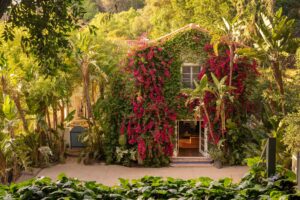Elegant Mediterranean home with terracotta roof, tropical plants, and scenic hillside view.