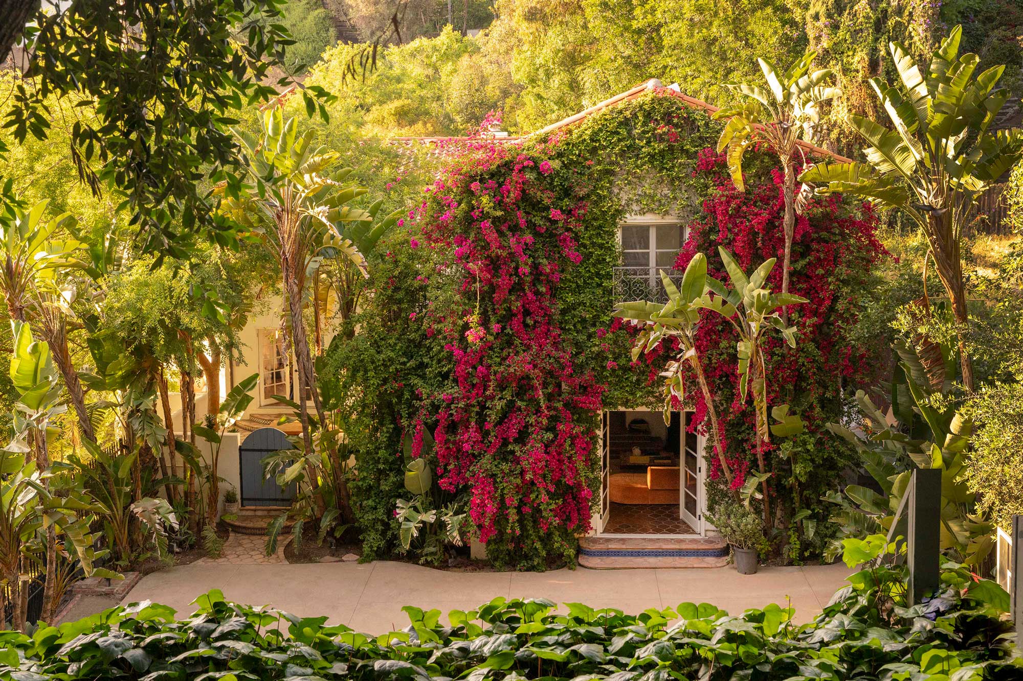 Elegant Mediterranean home with terracotta roof, tropical plants, and scenic hillside view.