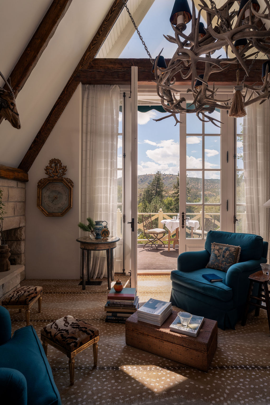 A-frame living room with an antler chandelier and French doors open to a mountain-view balcony