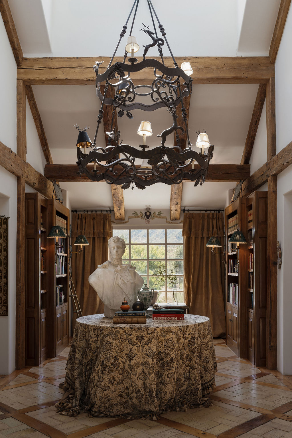 Double-height library hall with a wrought-iron stag chandelier, plaster bust and mountain-view window